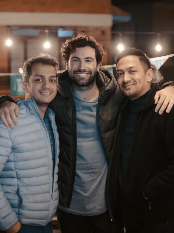 Outside&#039;s three founders, Atulya, Vincent, and Sujan, smiling. Vincent has his arms wrapped around the other two.